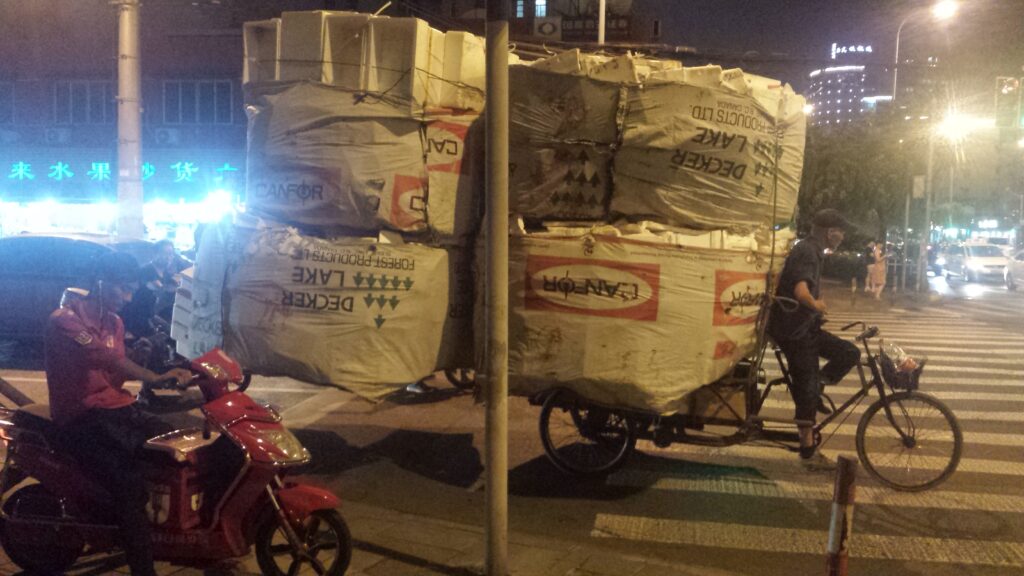 man rides tricycle carrying styrofoam (scouter in the foreground)