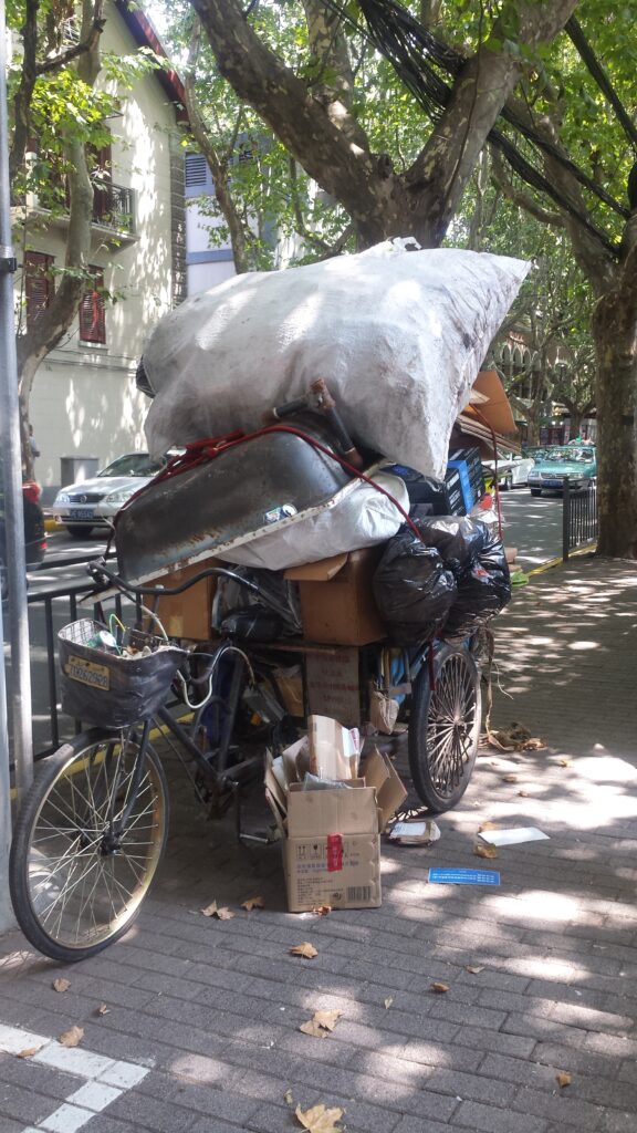 Tricycle parks on a sidewalk with personal belongings.