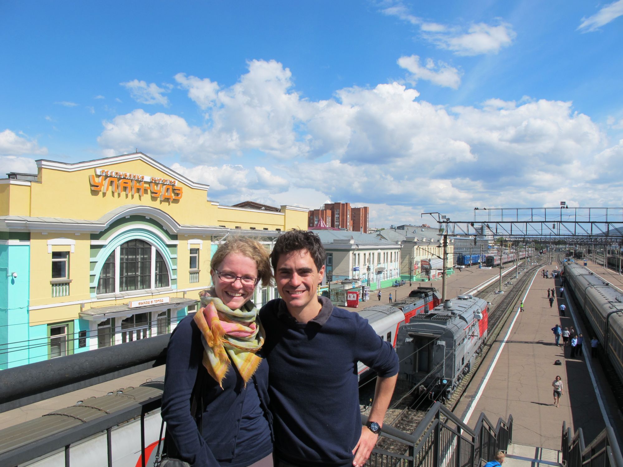 two people stand together in front of a train station
